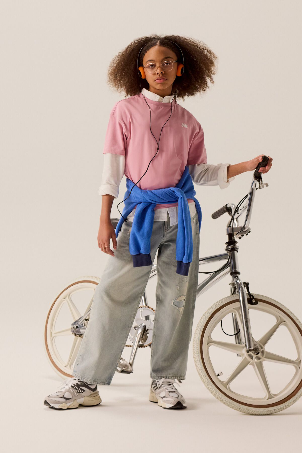 Young kid standing in front of a bike wearing blue jeans and a pink shirt. 